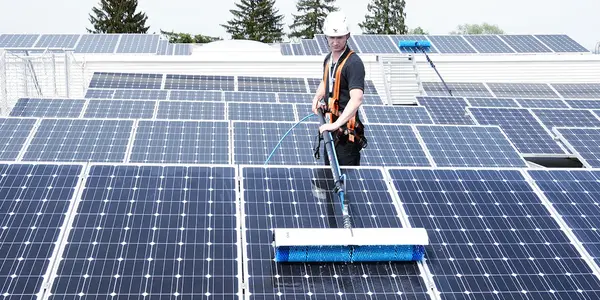 Fachkraft reinigt Solaranlage auf einem Dach für optimale Photovoltaik-Leistung und Effizienz.