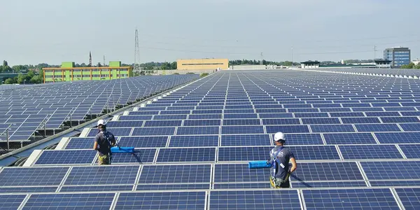 Zwei Arbeiter reinigen eine große Photovoltaikanlage auf einem Flachdach bei sonnigem Wetter.