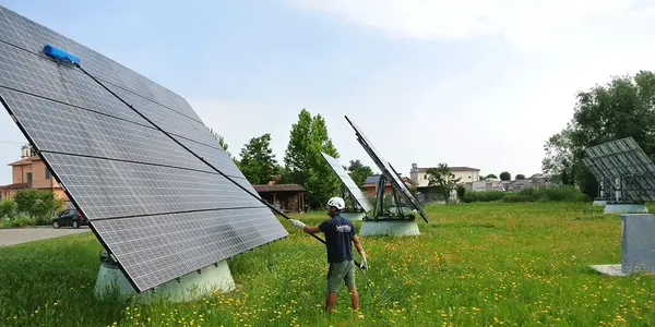 Ein Techniker reinigt Solarpanels auf einer Photovoltaikanlage im Grünen für mehr Effizienz.