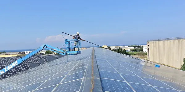 Arbeiter reinigt große Solaranlage auf einem Industriedach mit Hubarbeitsbühne bei Sonne.