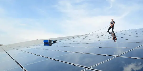 Ein Arbeiter reinigt große Solaranlage mit Spezialgerät unter blauem Himmel für Photovoltaik Wartung.